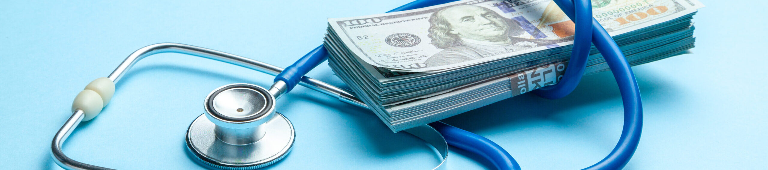 Stack of cash dollars and stethoscope on blue background. The concept of medical strechevka or expensive medicine, doctors salary